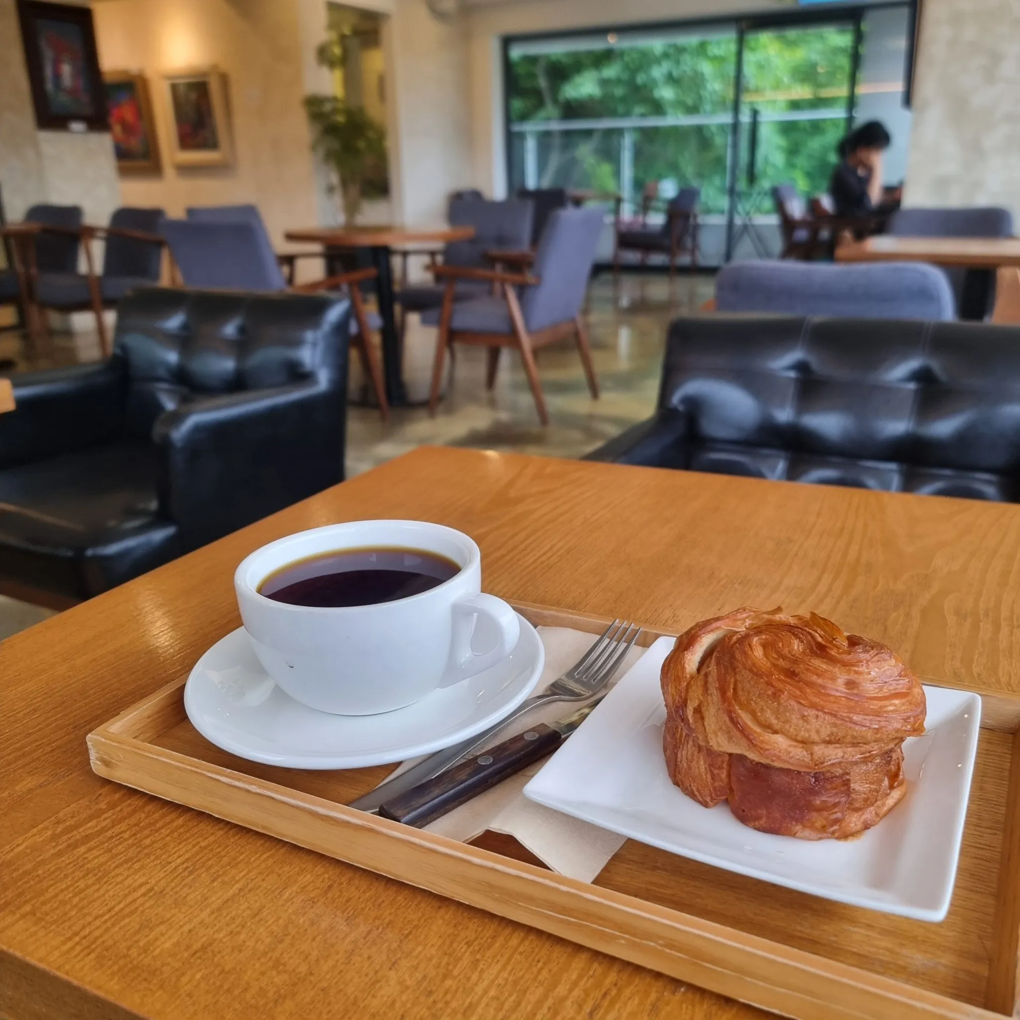 Café con leche y un croissant sobre una bandeja de madera, en un café acogedor con luz cálida