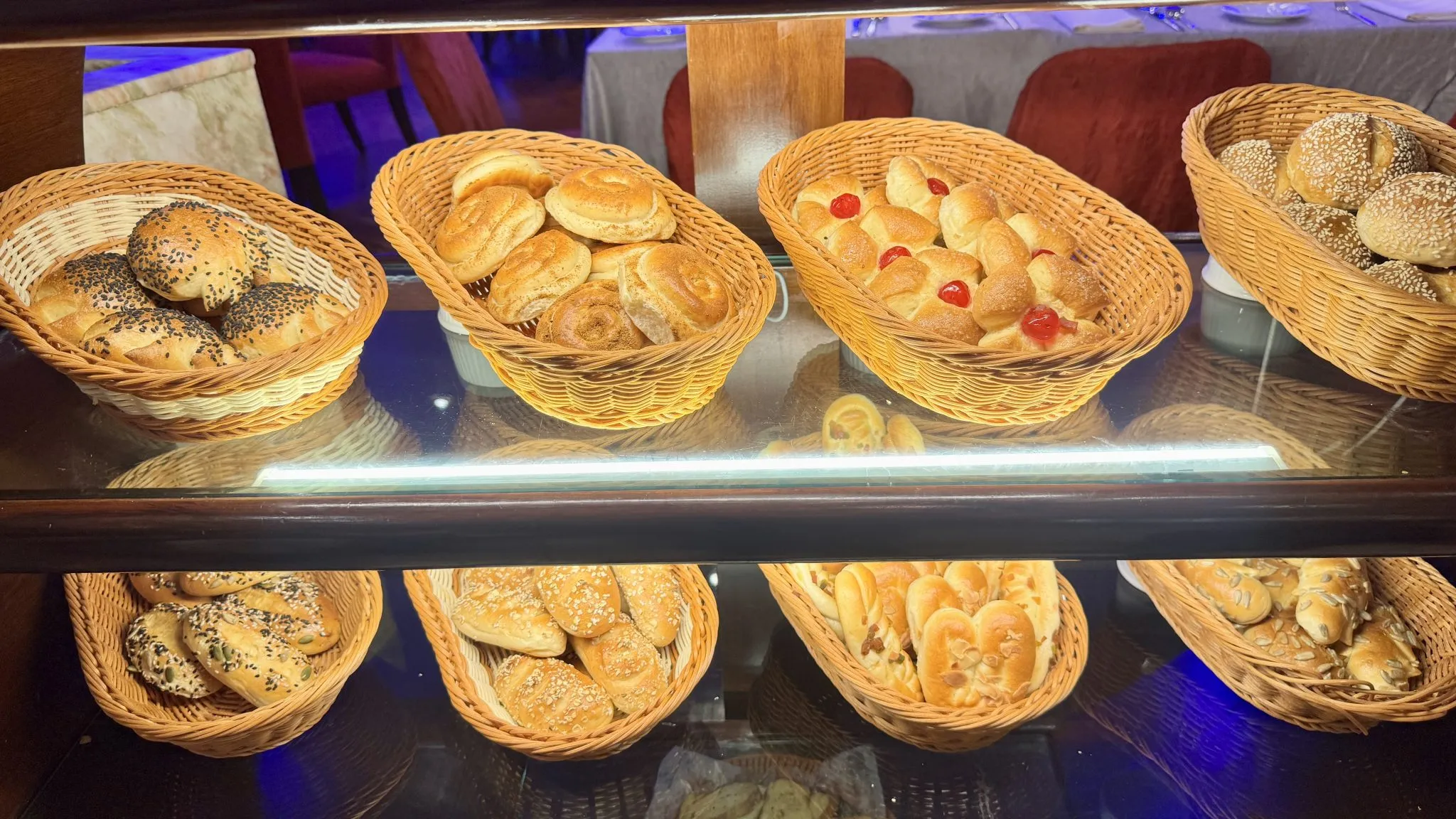 Estante de panadería con variedad de panes frescos, algunos con semillas, en canastos de mimbre